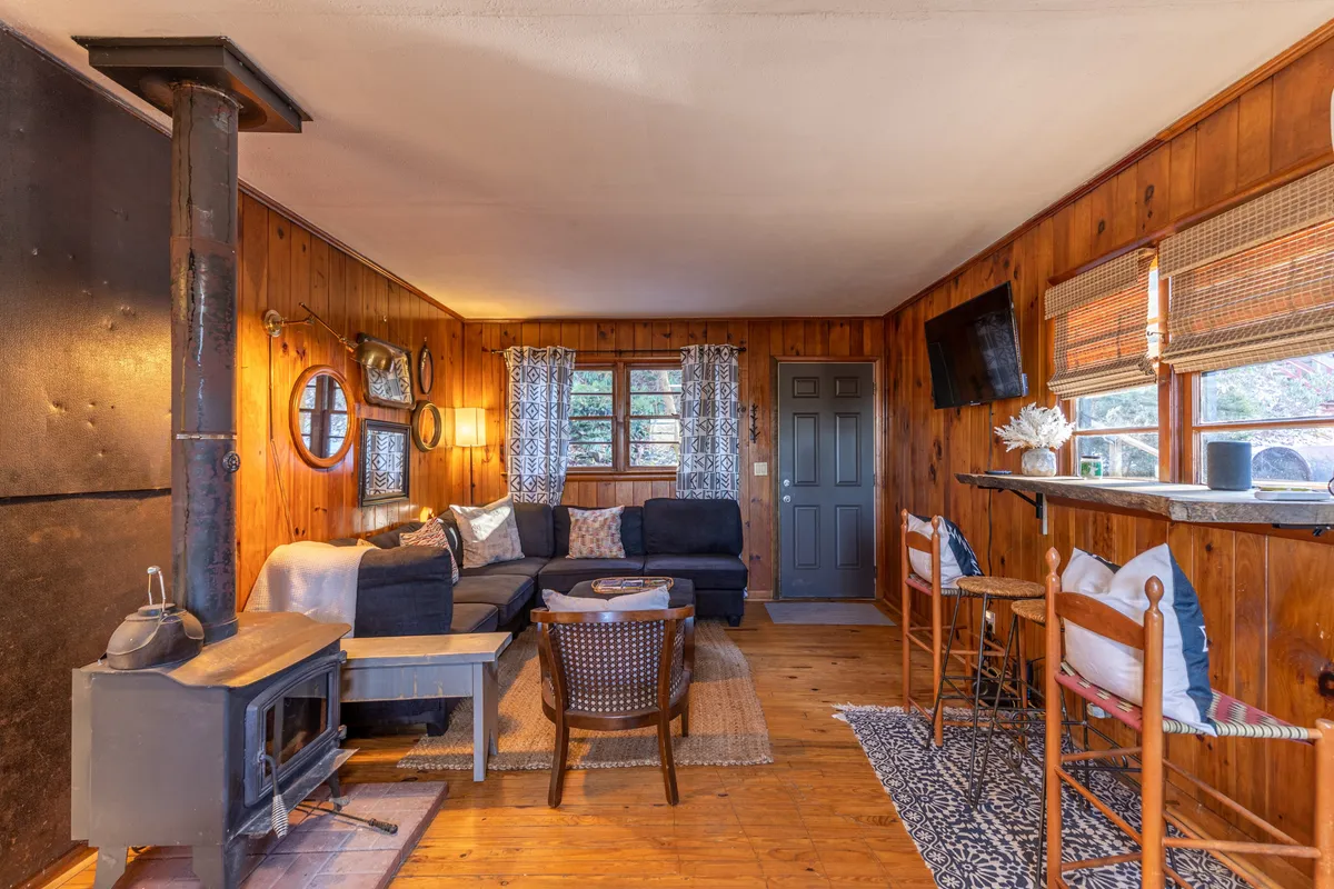This image centers on the living room's wood-burning stove, plush sectional sofa, bar seating, and decorative touches like mirrors. The arrangement is inviting and conducive to gathering, relaxation, and cozy evenings by the fire. The overall feeling is warm and welcoming, showing a space designed for both comfort and togetherness.