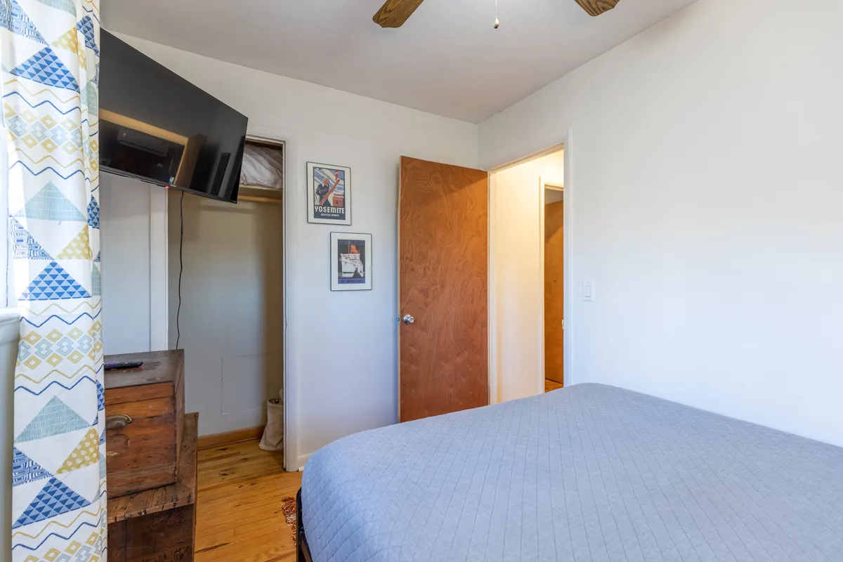 A warmly lit bedroom featuring a plush bed, inviting décor, and glimpses of framed artwork and a television. The scene suggests a comfortable spot to unwind, whether after exploring downtown Boone or enjoying a quiet movie night in.